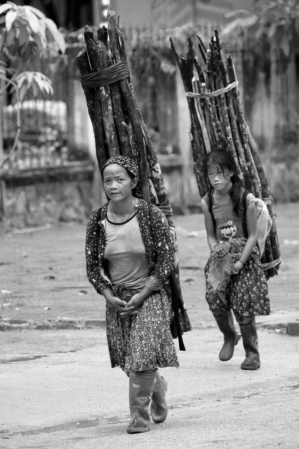 grayscale photography of two women carrying woods on back