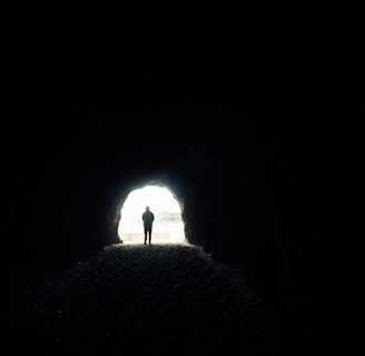 a person standing in a dark tunnel with a light at the end