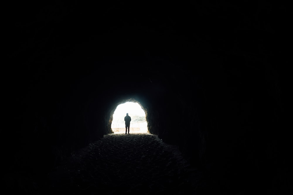 a person standing in a dark tunnel with a light at the end