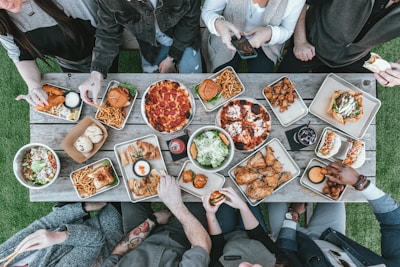 Outdoor picnic scene featuring people sharing hickory smoked burgers around a wooden table.