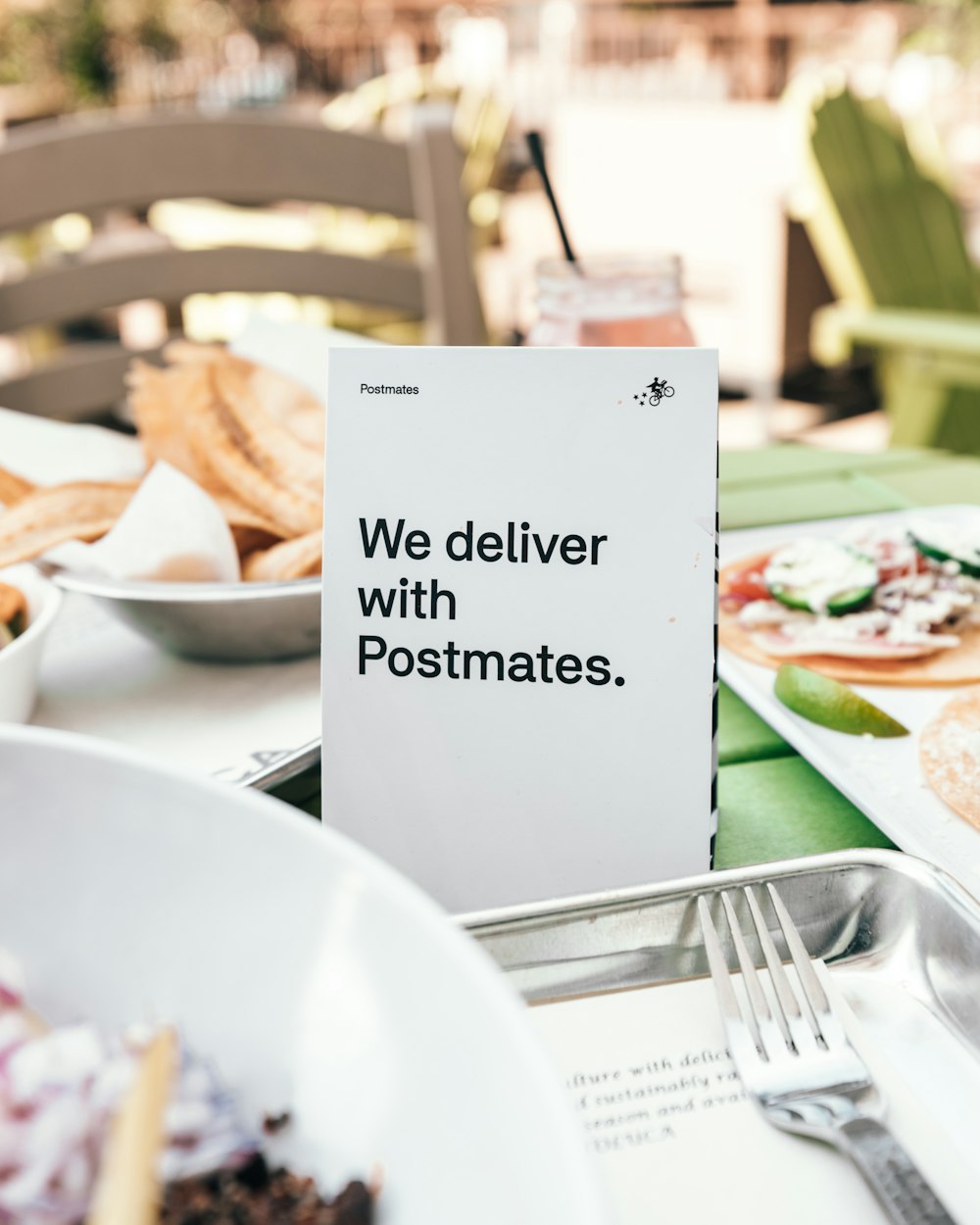 fotografía de enfoque selectivo de Entregamos con el letrero de Postmates en la mesa junto a las bandejas de comida
