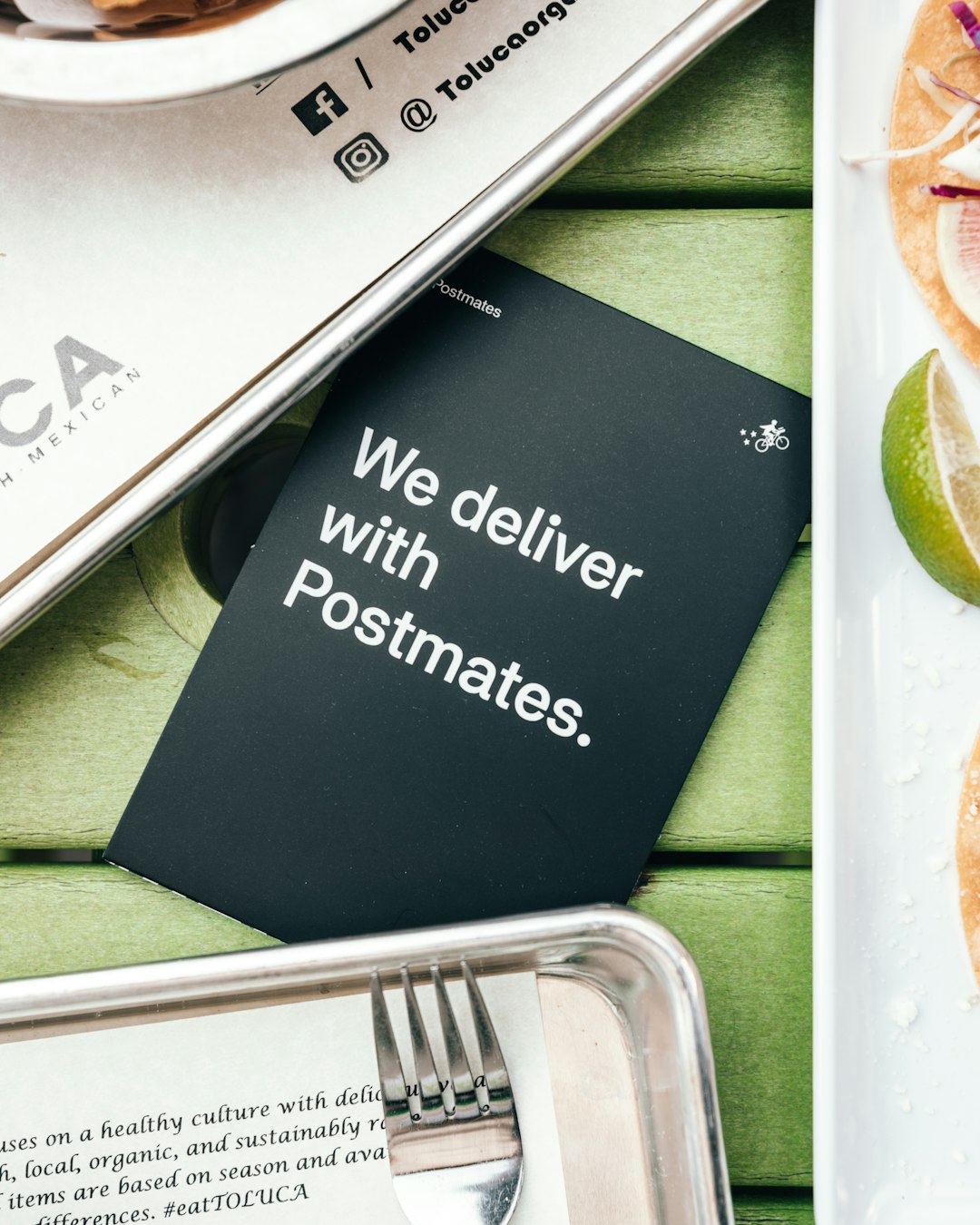 We deliver with Postmates sign on table beside trays