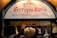 A shop sign displays the name 'Ferrigno Marco' with the phrase 'Arte in Terracotta Napoletana' below. The background features a lit chandelier and terracotta figurines of angels against a brick wall.