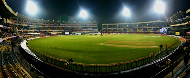 A cricket stadium under floodlights with players celebrating a last-ball win