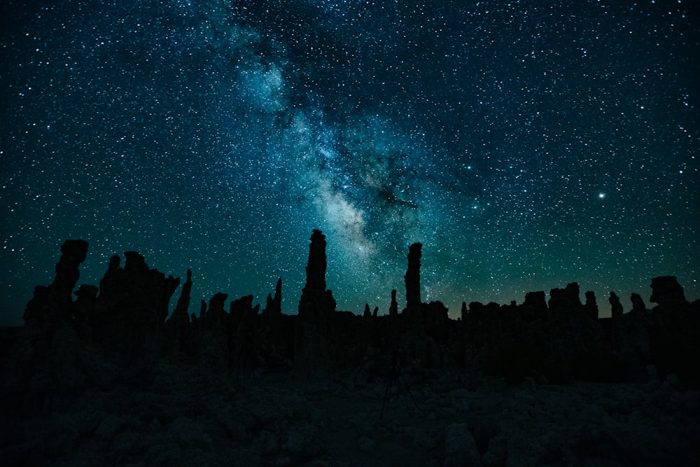 O céu noturno está cheio de estrelas e silhuetas de formações rochosas