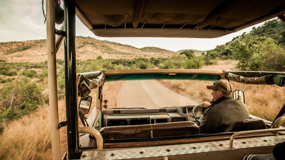 man driving vehicle on road between green plants