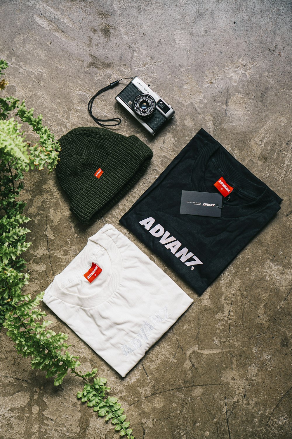 two black and white Advanz shirts beside knit cap and camera