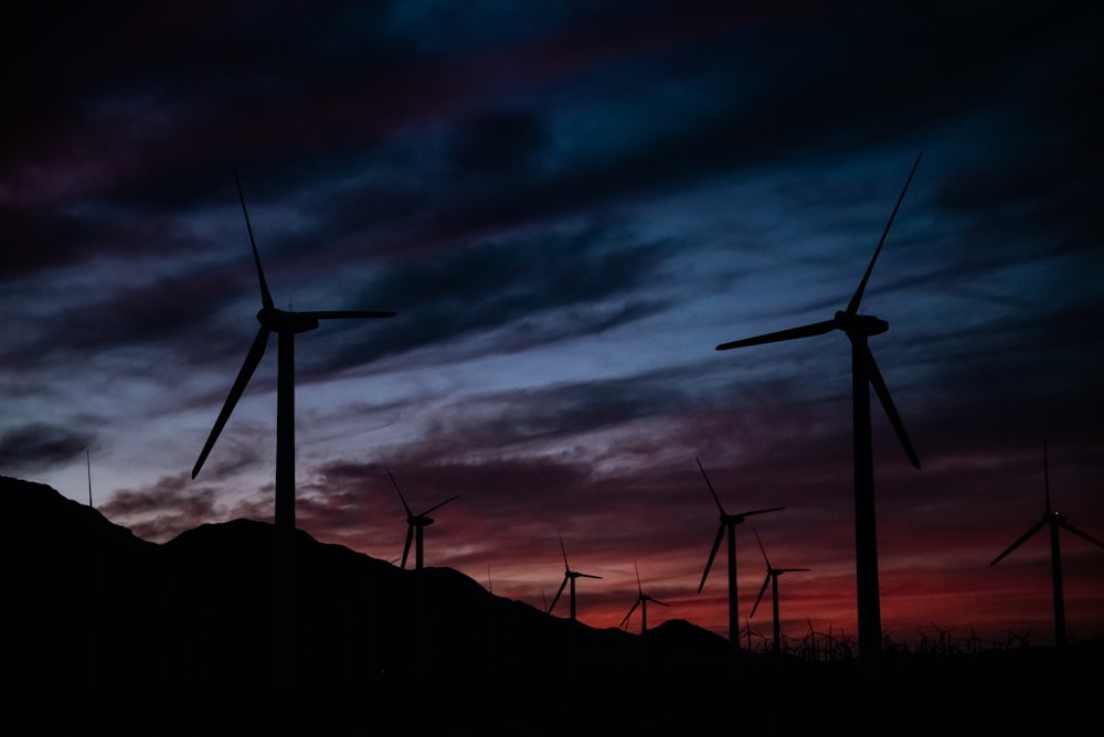 a group of windmills are silhouetted against a sunset