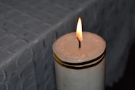 Partial view of a textured fabric napkin beside a glowing candle in a dim room.