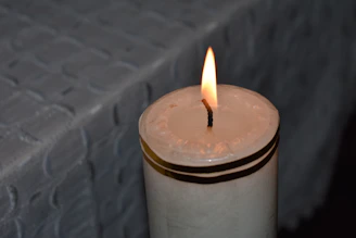 Partial view of a textured fabric napkin beside a glowing candle in a dim room.