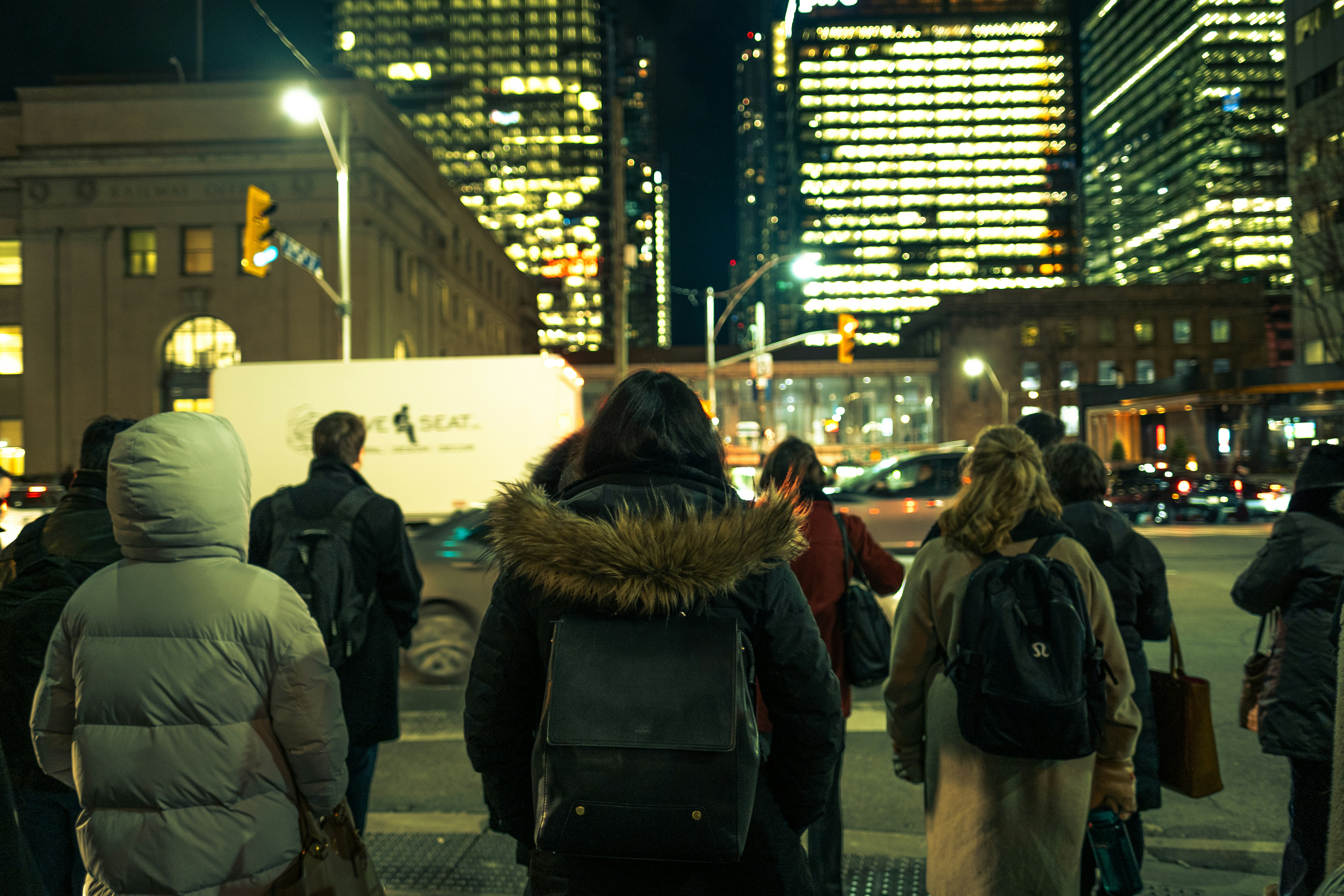 Pedestrians bundled in winter coats crossing a snowy city street at night in Canada