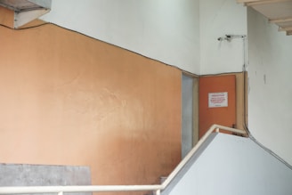 A beige-colored interior wall with a staircase leading up to a closed door. There are signs on the door, indicating it might be an area restricted to staff. A surveillance camera is mounted nearby.