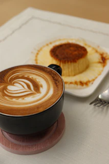 Close-up of a steaming cup of artisan coffee next to a delicate dessert on a sleek black tray