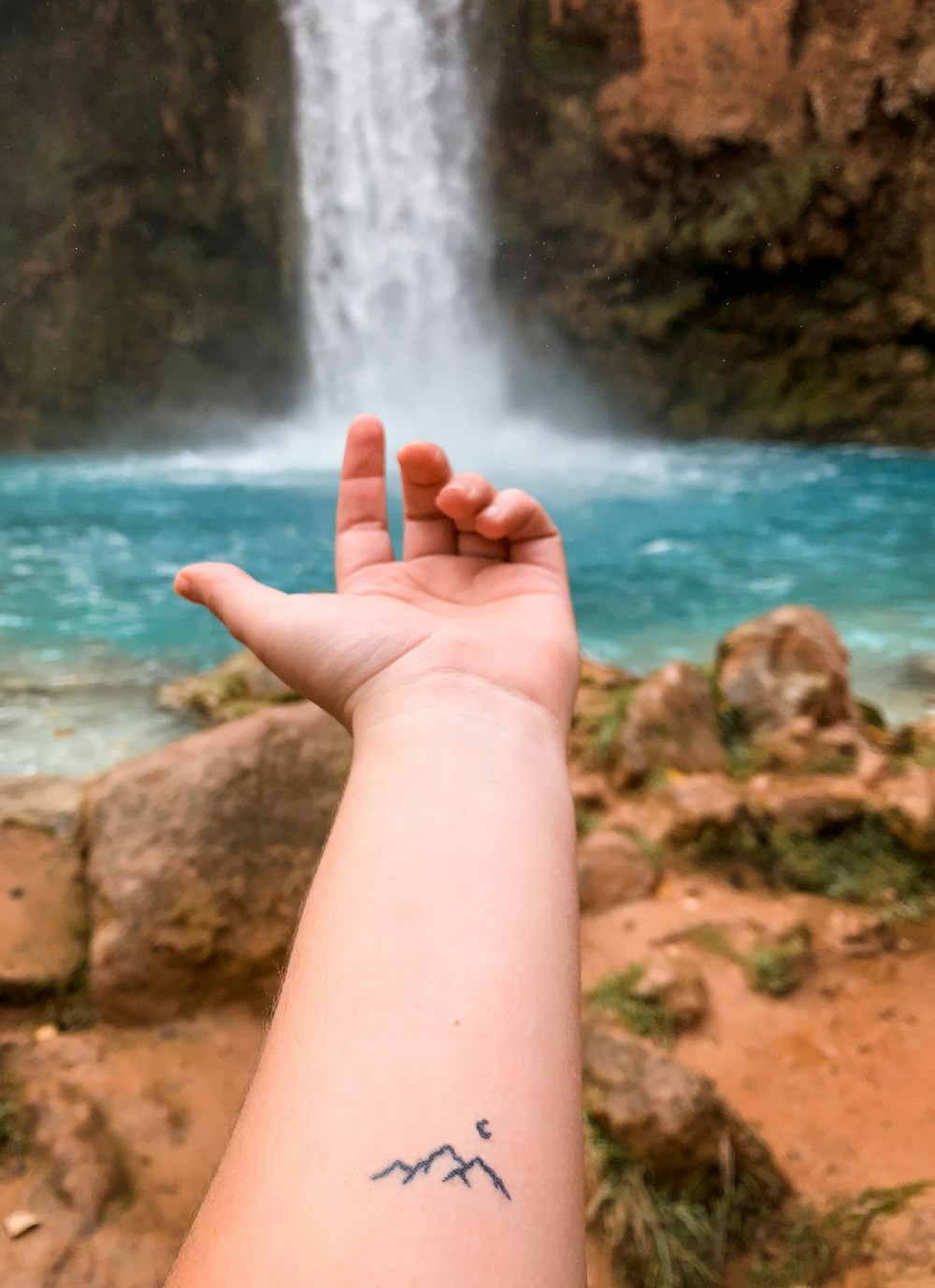 a person's arm with a small tattoo of mountains and a waterfall