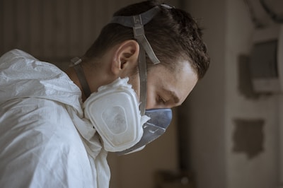 A person wearing protective gear, including a white coverall and a respirator mask, appears to be focused and working in a potentially hazardous environment. The setting suggests a professional or industrial context.