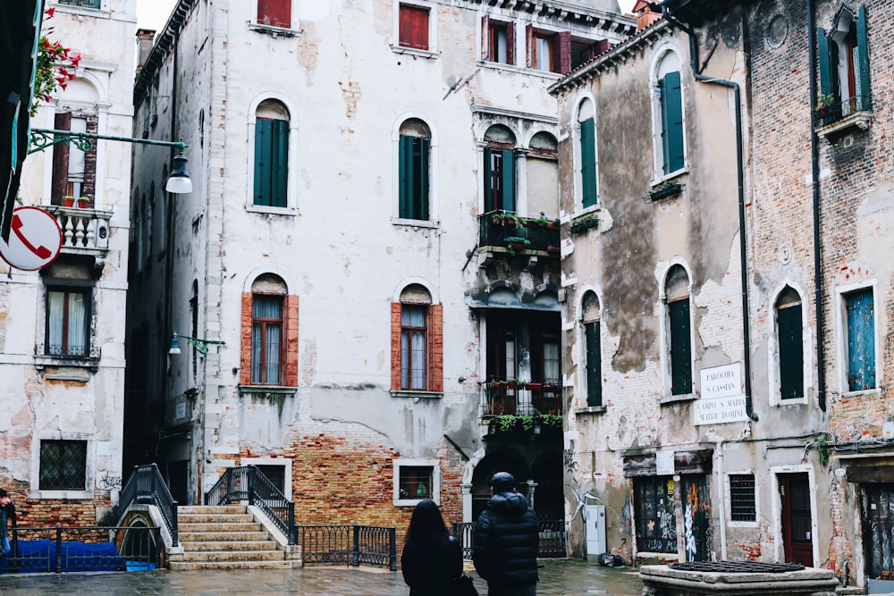 a couple of people walking down a street next to tall buildings