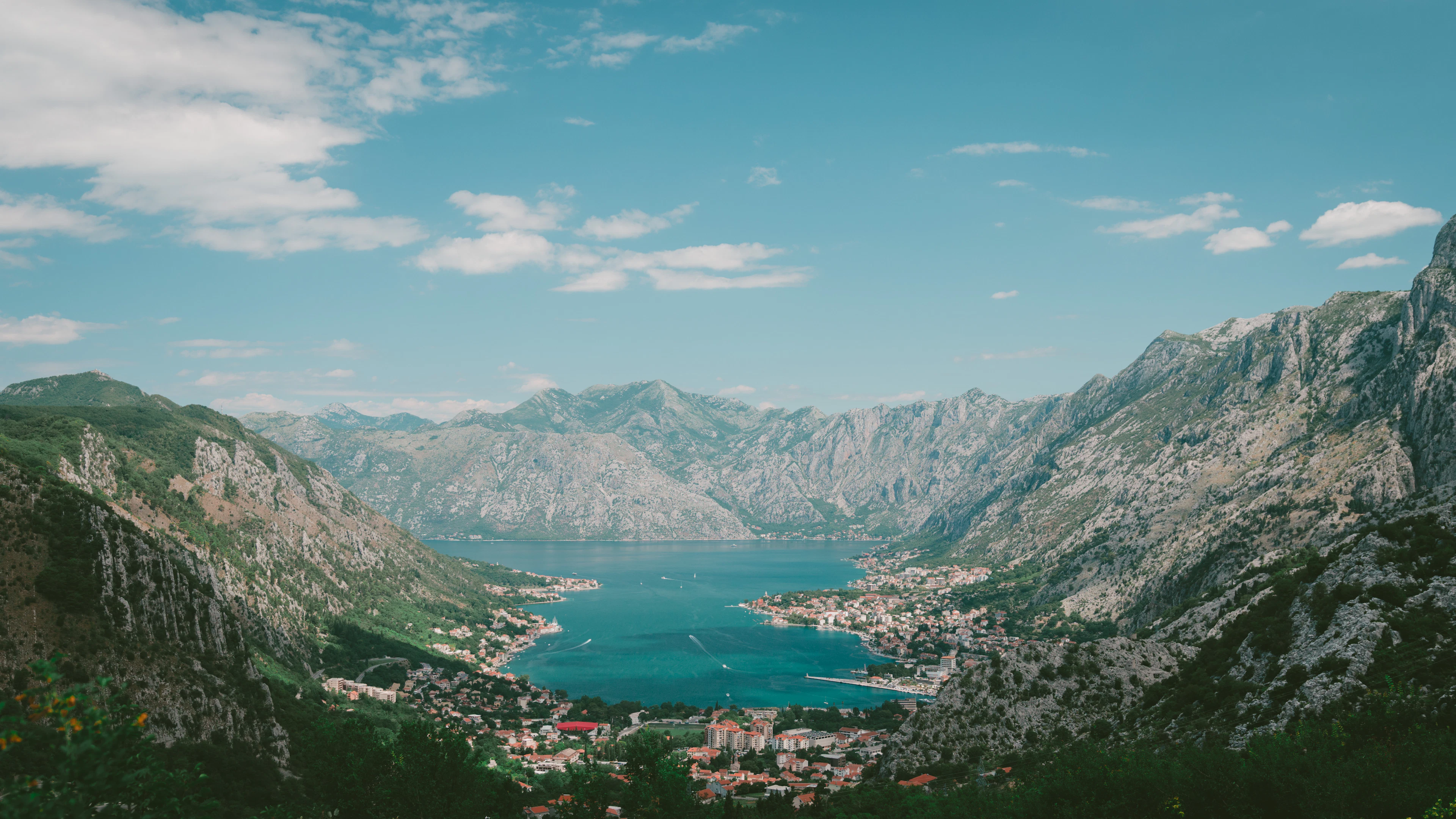 A panoramic aerial view of a winding blue bay surrounded by steep green mountains.
