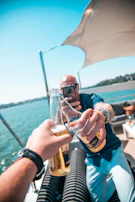 Candid shot of friends cheering with drinks aboard a boat, smiles bright under a terracotta sky.