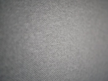 A close-up view of a textured fabric surface with a subtle geometric pattern. The fabric appears to have small, evenly distributed dots creating a sense of depth and dimensionality.