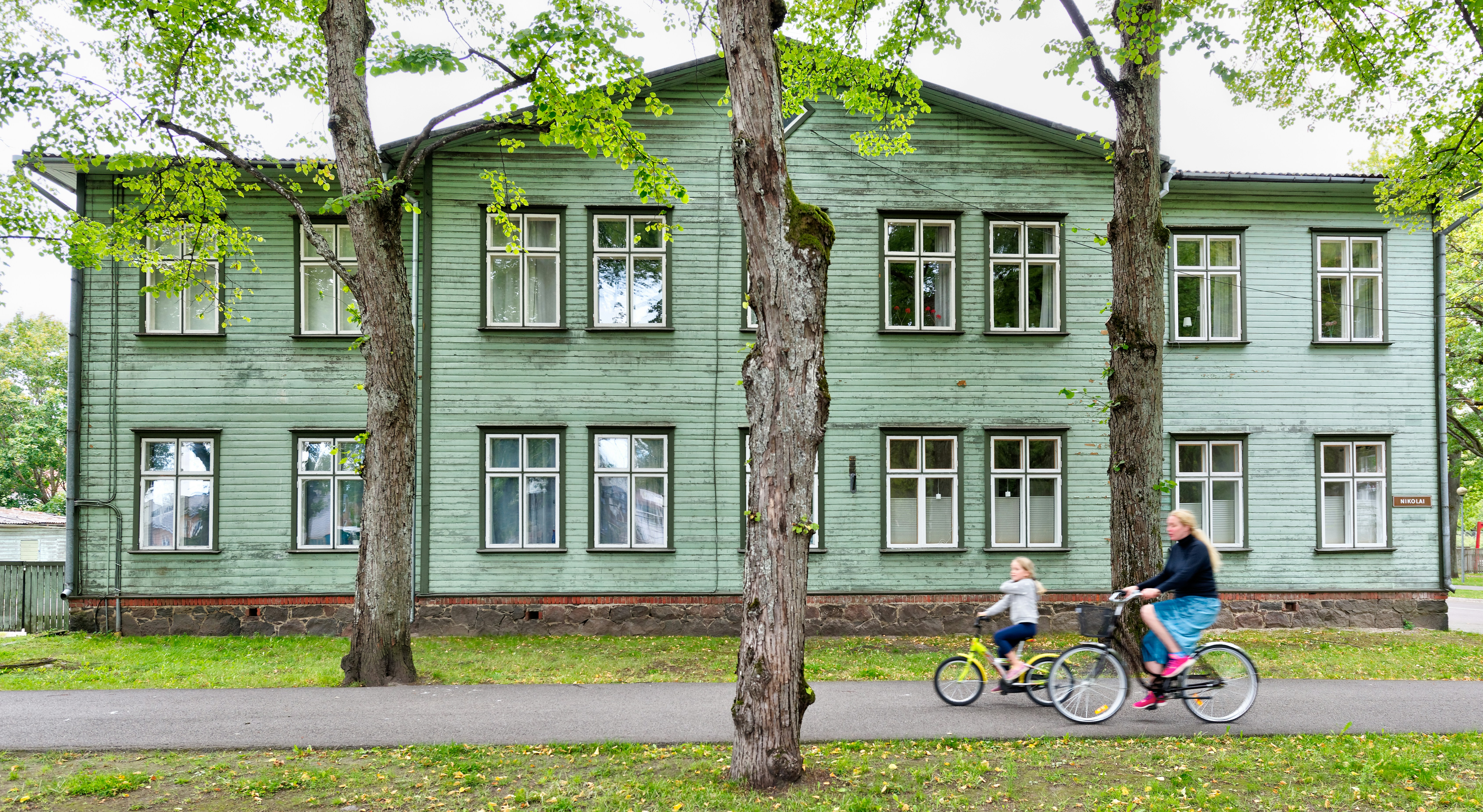 two cycling people passing gray wooden house