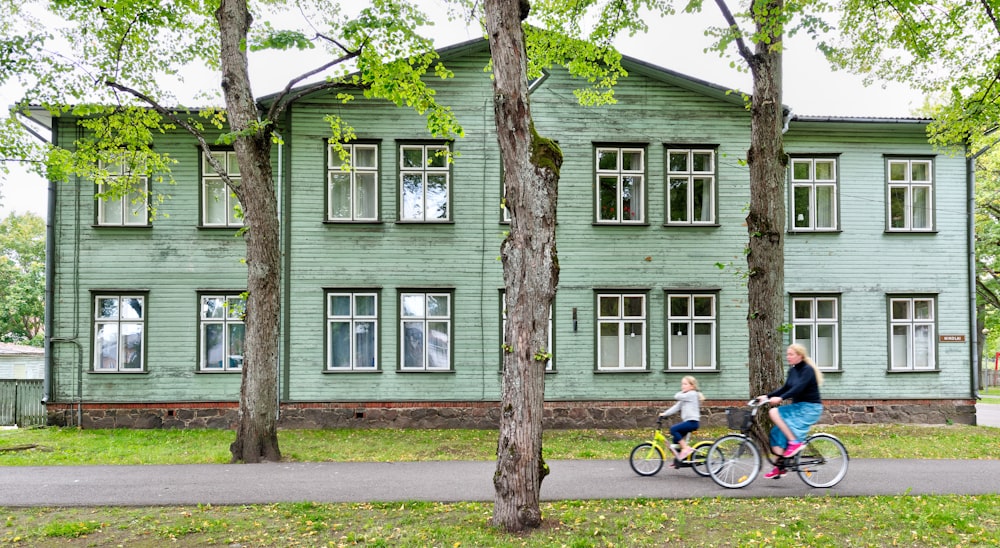 two cycling people passing gray wooden house