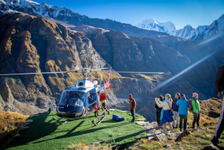 Passengers boarding a helicopter at a scenic mountain helipad surrounded by pine trees.