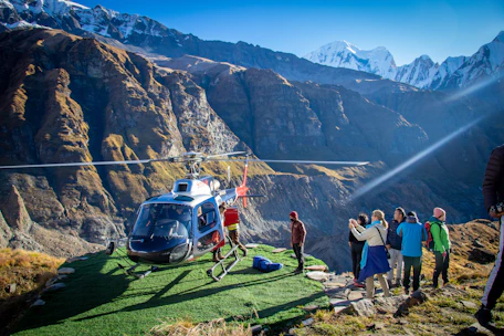 Passengers boarding a helicopter at a scenic mountain helipad surrounded by pine trees.