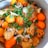 A pot filled with a vibrant stew comprising chicken pieces, whole orange tomatoes, and topped with fresh garnish like cilantro and chopped green onions. The ingredients are cooked in a rich broth that seems to enhance the color of the vegetables and meat.