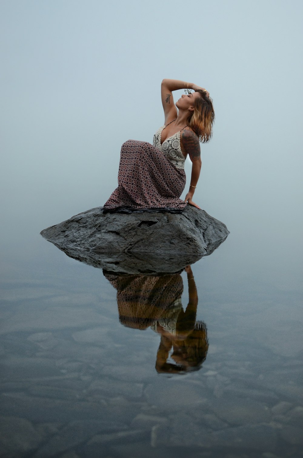a woman sitting on top of a rock next to a body of water