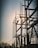 A silhouetted structure of metallic electrical components set against the backdrop of a setting or rising sun. The structure features tall vertical rods and various connected insulators, with the sun creating a bright glare through the framework. Bare trees are visible in the foreground, adding to the industrial setting.