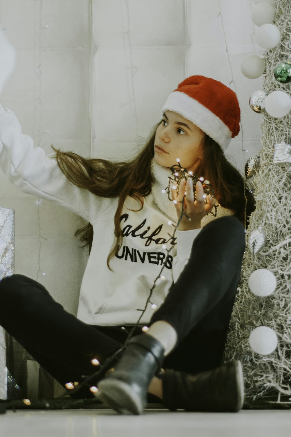 fotografía de enfoque selectivo de mujer sentada con sombrero de Papá Noel al lado del árbol de Navidad