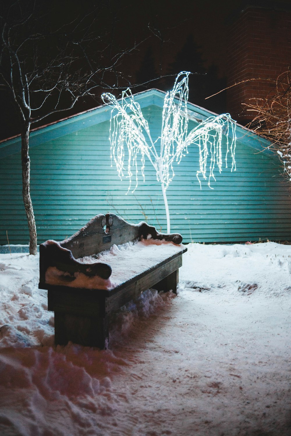 snow covered brown bench beside house