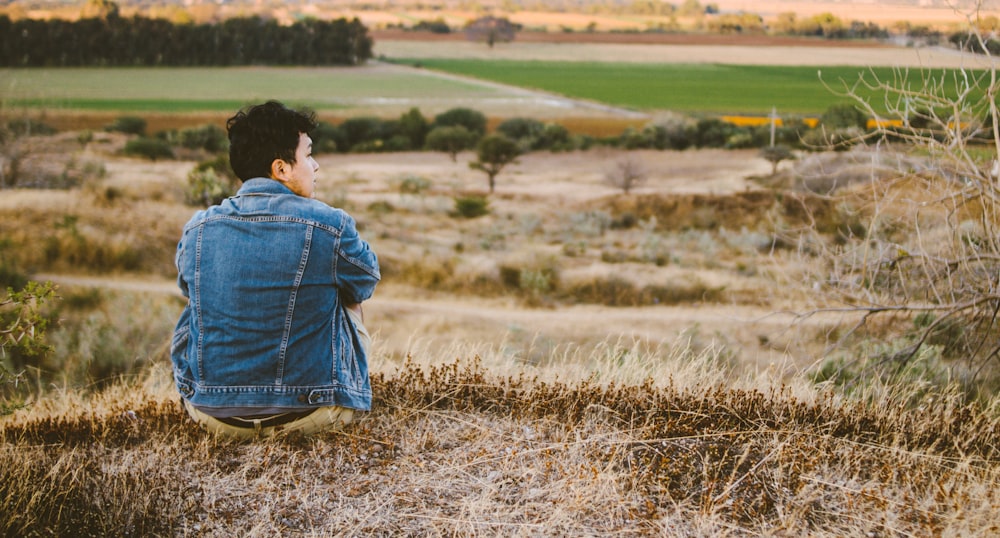 man wearing blue jacket sitting on the grass field