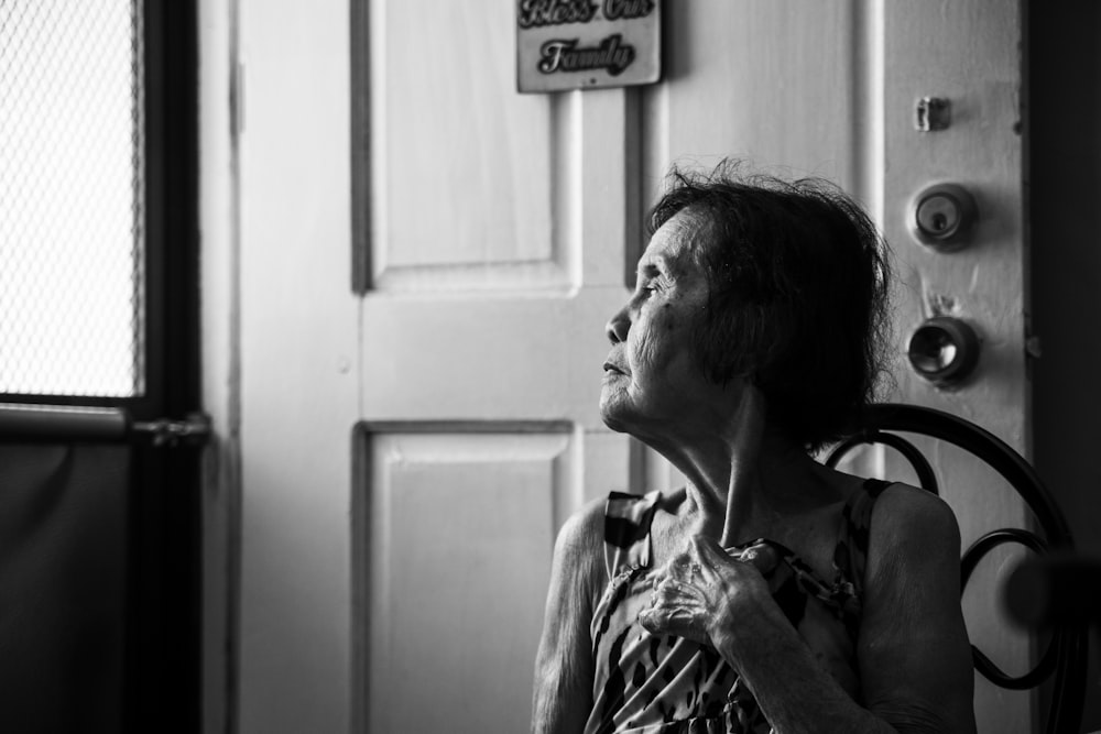 grayscale photography of woman beside door looking outside