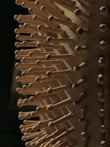 Close-up of a hairbrush with wooden bristles, each evenly spaced and protruding from a textured base. The lighting casts soft shadows, highlighting the natural wood tones and pattern of the brush.