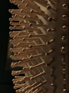 Close-up of a hairbrush with wooden bristles, each evenly spaced and protruding from a textured base. The lighting casts soft shadows, highlighting the natural wood tones and pattern of the brush.