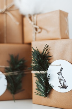 Several neatly wrapped gifts in brown paper, adorned with simple twine and decorated with sprigs of green foliage and rabbit illustrations on white tags. The setting has a minimalist and natural aesthetic.