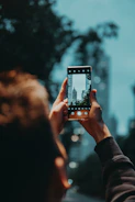 A person holding a smartphone outdoors with a cityscape in the background