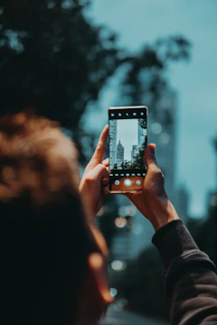 A person holding a smartphone outdoors with a cityscape in the background