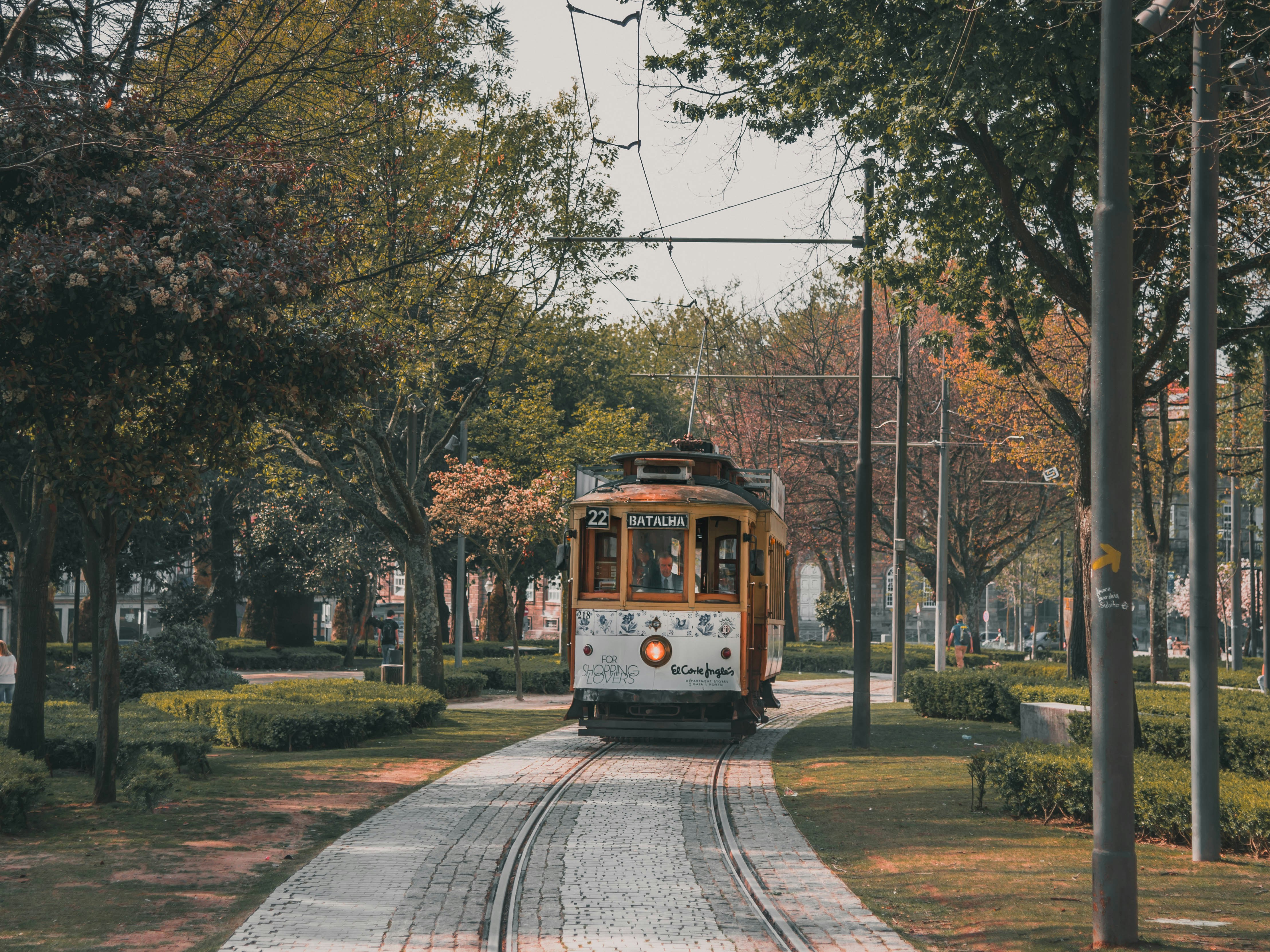 brown and white tram between trees, One of the most enjoyable tourist activities of Porto is a ride on one of the historic trams (Electrico in Portuguese). These delightful trams date from a by-gone era, when vehicles were built with character, and have polished wood interiors, brass controls and dials, and a clanging bell to stop the tram.</p><p>In any other city (apart from Lisbon!) these trams would be hidden away in a museum, but in Porto they rattle and screech through the city, even being forced to climb some of the city’s steepest hills.