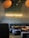 A cozy interior of a restaurant with gray upholstered seating and wooden tables. The wall displays a neon sign that reads 'RAMEN POWER,' creating a warm atmosphere. Overhead lighting adds to the soft, inviting ambiance.