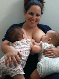 A candid photo of a nurse gently holding her twins, smiling warmly in a cozy home setting.