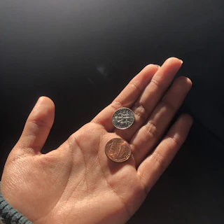 A warm hand gently giving coins to another beneath a glowing, golden sky.