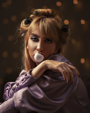 A fierce woman in a pink faux fur coat blowing a big bubblegum bubble, with smeared red lipstick and leopard print background.