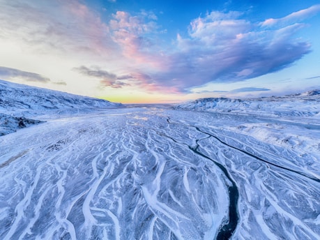 A sweeping aerial view of Greenland's icy fjords under a soft pink Arctic sky.