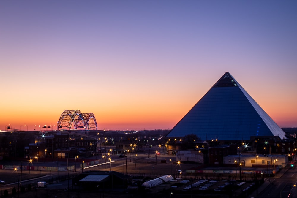 a sunset view of a large pyramid with a ferris wheel in the background