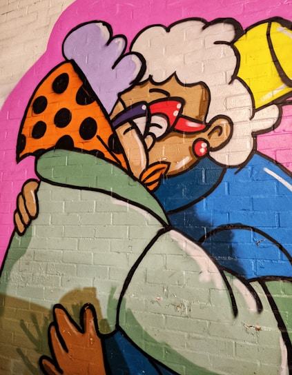 A vibrant graffiti artwork depicting two cartoonish characters embracing. One character has white curly hair, oversized red glasses, and wears a blue outfit, while the other is adorned with a spotted orange hat and green coat. The background is a bold pink color, adding to the lively and colorful nature of the artwork.