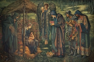 A serene scene depicting several figures in robes around a central seated woman holding a child. An angel with wings stands behind, holding a glowing object. The setting appears to be outdoors with trees and a rustic wooden structure resembling a stable. The figures are engaged in a moment of offering or reverence, with some holding elaborate items, and a crown is placed on the ground.