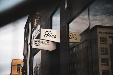 A street view of a modern building showcasing a dental office sign with the text 'Sierra Dental & Orthodontics'. The dark facade contrasts with reflective windows that mirror the surrounding urban landscape.