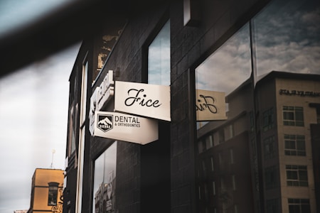 A street view of a modern building showcasing a dental office sign with the text 'Sierra Dental & Orthodontics'. The dark facade contrasts with reflective windows that mirror the surrounding urban landscape.